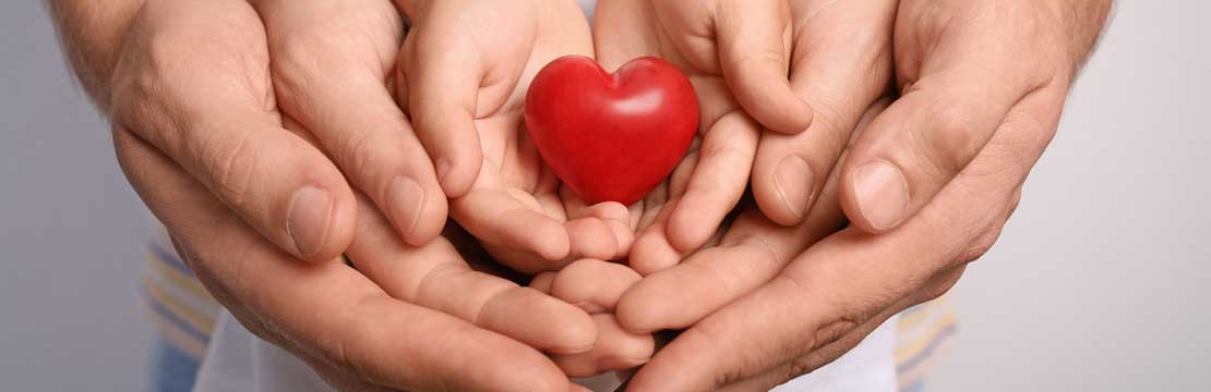 Close up of a family holding small red heart in their hands.